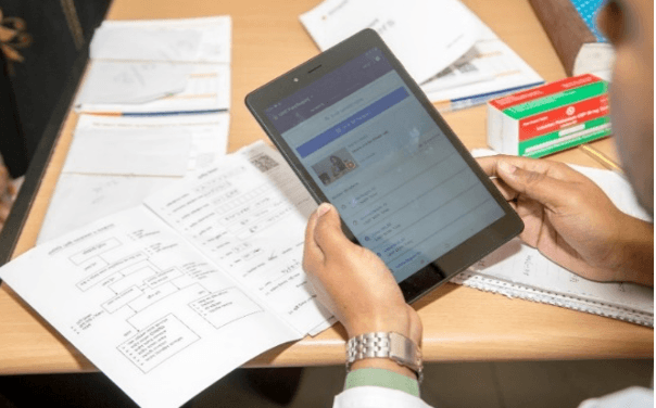 A health worker entering a patient record on a tablet beside the paper register
